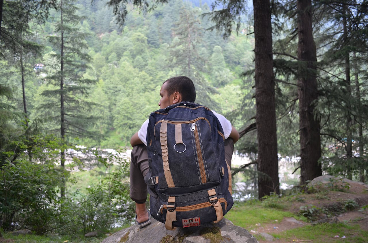Backpacker sitting on a rock, enjoying the scenic forest and river view during a daytime hike.